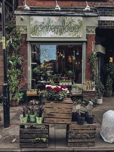 The exterior of 'Northern Flower,' a flower shop with a vintage-style signboard, displaying the shop's name in elegant script surrounded by green floral illustrations. In front of the shop, there are 